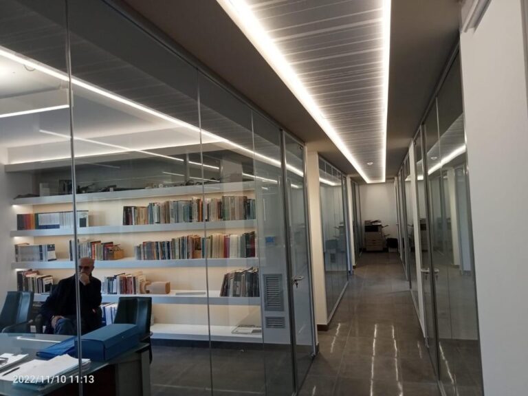 Corridoio ufficio con pareti di vetro e scaffali di libri.